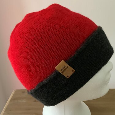 seitliche Ansicht einer rot-grauen gestrickten Mütze mit umgeschlagenem Bund und kleinem Label auf weißer Schaufensterpuppe