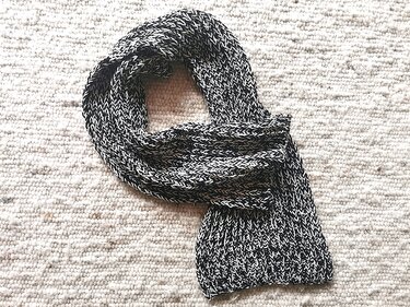 Schwarz-weißer gestrickter Schal mit Rippenstruktur auf hellem Teppich