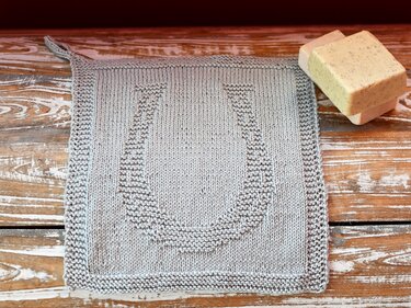 Hellgraues gestricktes Quadrat mit geprägtem Hufeisen-Relief, krauser Rand und Aufhängeschlaufe