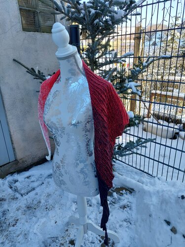 Gehäkeltes halbrundes Tuch in Rot und Schwarz auf einer Schneiderpuppe im Schnee.