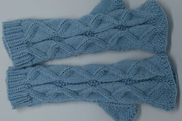 Hellblaue gestrickte Armstulpen mit Zopfmuster und Rippbündchen, liegend.
