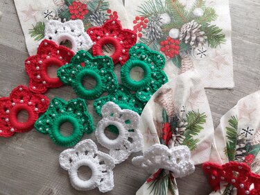 Gehäkelte Serviettenringe in Rot, Grün und Weiß mit Perlen auf weihnachtlichen Servietten und Holzuntergrund.