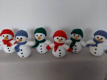 Sechs gehäkelte Schneemänner mit bunten Mützen und Schals nebeneinander