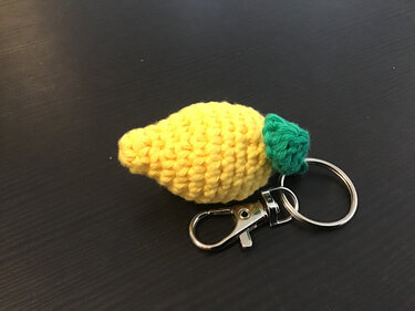 Kleiner gelber Zitronenanhänger aus festen Maschen mit grünem Blatt an Schlüsselring