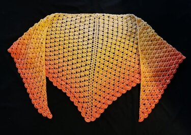 Gehäkeltes Dreieckstuch mit Farbverlauf von Gelb nach Orange auf dunklem Hintergrund