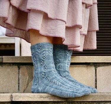 Wadenlange graublaue Socken mit Zopf- und Lochmuster auf einer Treppenstufe