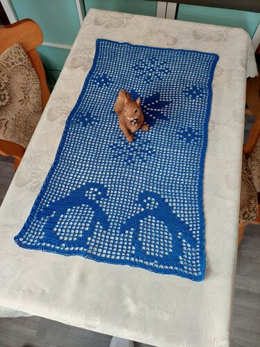Blauer Filet-Tischläufer mit Vogelmotiven und Eichhörnchen-Figur auf weißer Tischdecke