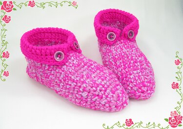 Zwei gehäkelte pink-weiße Hausschuhe mit fuchsiafarbenen Umschlägen und Knöpfen auf weißem Hintergrund.