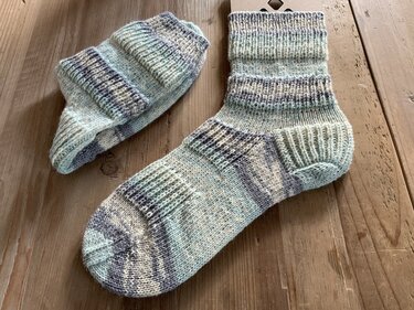 Nahaufnahme zweier handgestrickter Kurzsocken mit geformter Ferse und Rippenbündchen auf Holz