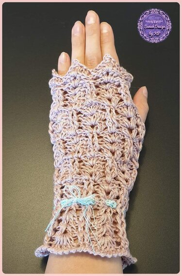 Hand mit gehäkelter, fingerloser Damenstulpe in hellem Rosa mit blauem Zierband