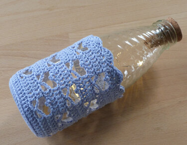 Windlicht aus Glasflasche mit hellblauer Häkelhülle und Lichterkette
