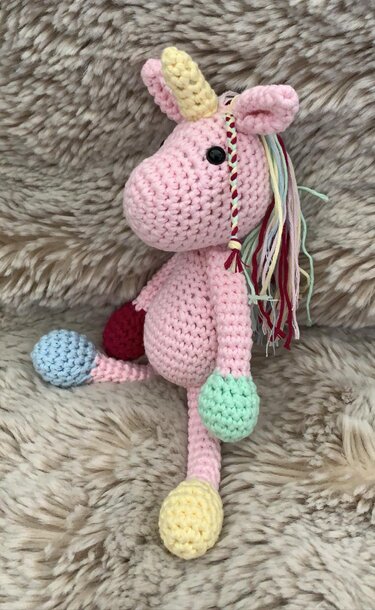 Rosa gehäkeltes Amigurumi-Einhorn mit gelbem Horn und mehrfarbiger Mähne