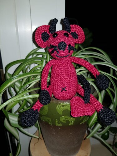 Sitzende rote Amigurumi-Teufelsmaus mit schwarzen Details und Herz am Schwanz