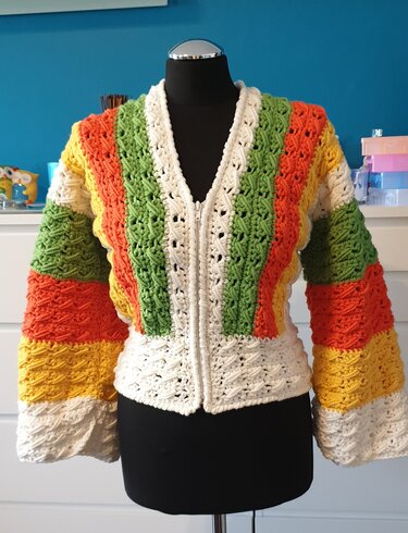 Bunt gestreifte Häkeljacke in Grün, Orange, Gelb und Weiß mit Reißverschluss auf einer schwarzen Schneiderpuppe.