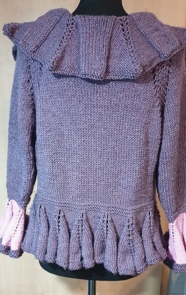 Rückenansicht einer fliederfarbenen gestrickten Damenjacke mit breitem Volantkragen, gefaltetem Rüschensaum und rosa Manschetten auf einer Puppe