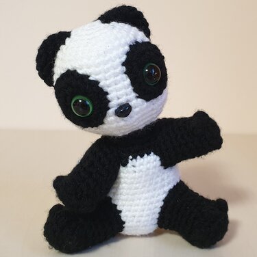 Gehäkelter schwarz-weißer Amigurumi-Panda mit grünen Augen, sitzt auf hellem Untergrund