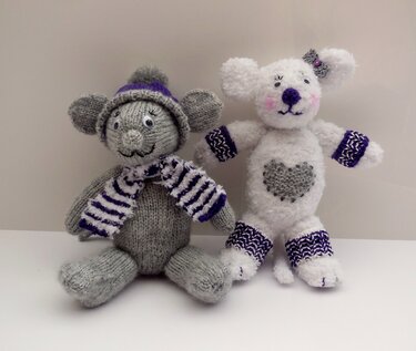 Zwei Amigurumi-Figuren: graue Maus mit Mütze und Schal, weißes Fantasietier mit Herz und gemusterten Bündchen.
