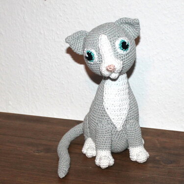 Gehäkelte graue und weiße Amigurumi-Katze mit türkisfarbenen Augen, sitzend