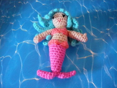 Gehäkelte Meerjungfrau-Puppe mit türkisfarbenem Haar und pinker Schwanzflosse auf blauem Hintergrund