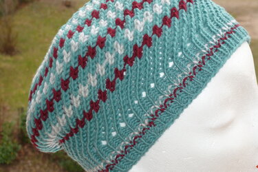 Gestrickte türkise Mütze mit weißem und dunkelrotem Herzmuster und gelochtem Rand.