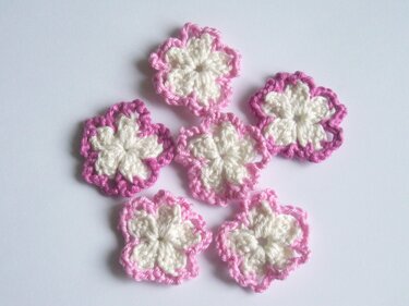 Sechs gehäkelte Blumen-Applikationen in Rosa und Weiß auf hellem Hintergrund