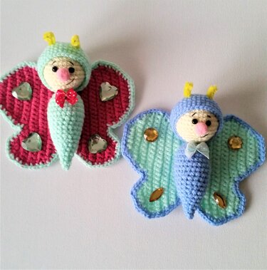Zwei Amigurumi-Schmetterlinge in Mint/Rosa und Blau/Mint mit verzierten Flügeln und kleinen Antennen