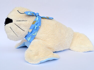 Cremefarbene Plüschrobbe mit schwarzer Nase, geschlossenen Augen und blauem Halstuch mit Seehundmotiven.