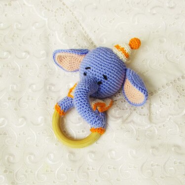 Light-blue crocheted elephant rattle and wooden teething ring with a party hat.
