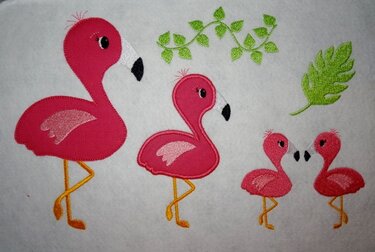 Vier gestickte Flamingos in verschiedenen Größen mit grünen Blättern auf hellem Stoff