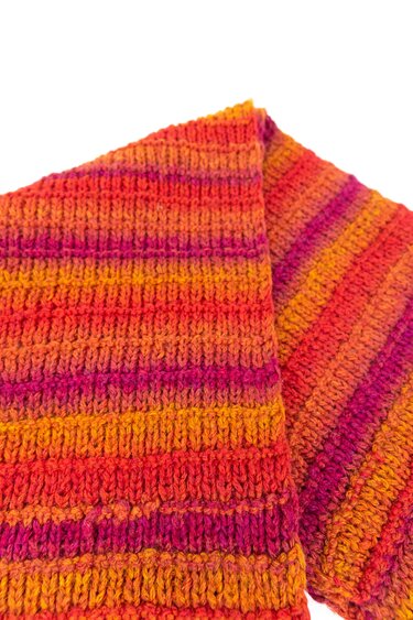 Nahaufnahme eines gestreiften Strickschals in Orange, Rot und Pink auf weißem Hintergrund.