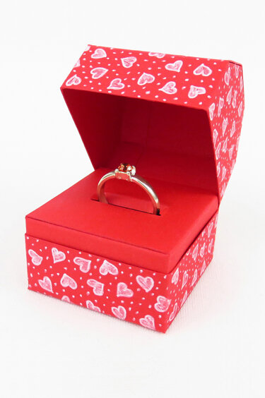 Offene rote Geschenkbox mit weißen Herzmotiven und einem Ring im Schlitz