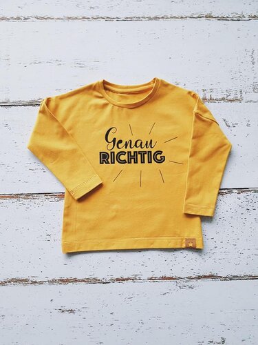 Gelbes Kinder-Langarmshirt mit schwarzem Schriftzug 'Genau Richtig' und radialen Strahlen