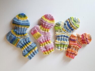 Vier Paar gestrickte Babysocken in bunten Streifen, von oben auf wei
m Grund