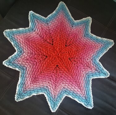 Gehäkeltes sternförmiges Deckchen in Rot‑Pink‑Blau mit weißem Zackenrand