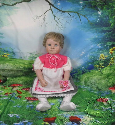 Gestricktes Babykleid an einer Puppe in Rosa, Weiß und Grau vor einem fantasievollen Hintergrund