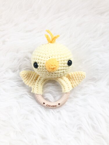 Gehäkelter gelber Küken-Beißring mit rundem Holzring auf weißem Plüsch