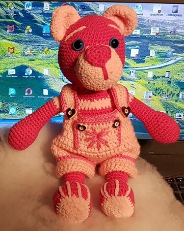 Gehäkelter Teddybär in Pink mit hellrosa Latzhose und herzförmigen Knöpfen