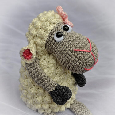 Gehäkeltes Amigurumi-Schaf mit cremefarbenem Puffstich-Körper, grauem Kopf, schwarzen Hufen und rosa Details