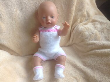 Puppe trägt weiß gestrickten Strampler mit rosa Rand und passende gestrickte Stiefelchen