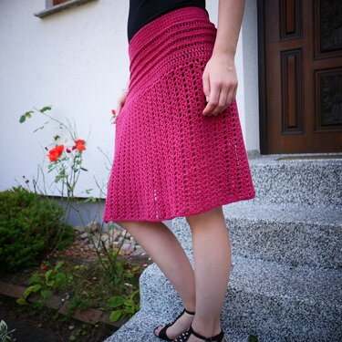 Gehäkelter himbeerfarbener A‑Linien‑Rock mit Lochmuster, getragen auf Steinstufen.