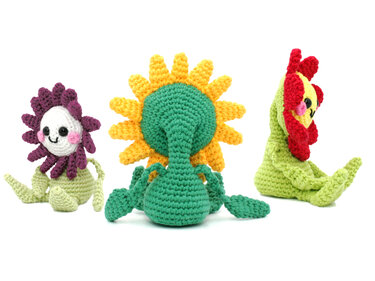 Drei bunte gehäkelte Blumenfiguren mit Gesichtern nebeneinander.