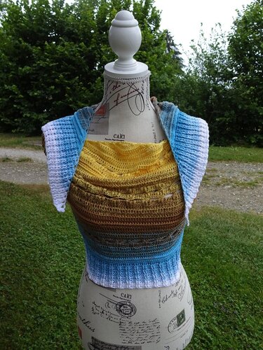 Gehäkeltes Halbrundtuch in Gelb, Braun, Blau und Weiß auf einer Schneiderpuppe im Garten