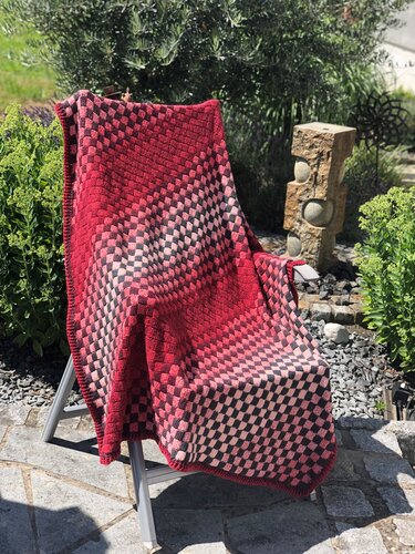 Gehäkelte Decke in Rot- und Rosatönen mit Schachbrettmuster auf Gartenstuhl