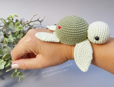 Gehäkelte Mini‑Schildkröte mit Flossen und rotem Herz am Handgelenk