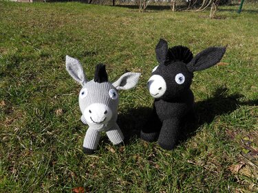 Zwei gestrickte Amigurumi-Esel, ein grauer und ein schwarzer, auf Gras