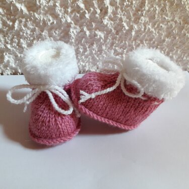 Kompaktes Paar gestrickter rosa Babyschuhe mit weißem Plüschrand und Bindekordel auf hellem Untergrund