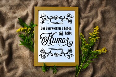 Gerahmtes Spruchbild ‚Das Passwort fürs Leben heißt Humor‘ mit floralem Rahmen auf braunem Stoff und gelben Blumen