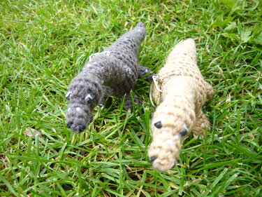 Zwei gehäkelte Amigurumi‑Dinosaurier‑Schlüsselanhänger in Grau und Beige auf grünem Gras