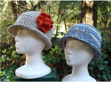 Two crocheted cloche hats on mannequin heads: beige with an orange flower, and blue-brown striped.