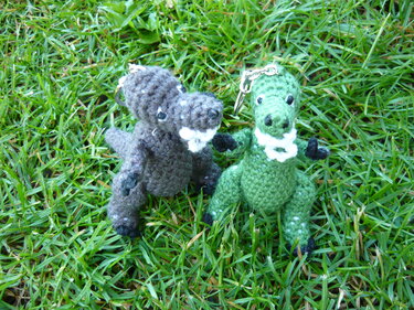 Zwei gehäkelte Dinosaurier‑Schlüsselanhänger, grün und grau, auf Gras
